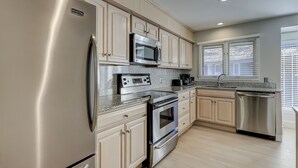 Una cocina moderna con electrodomésticos de acero inoxidable, armarios de madera clara y una ventana con persianas.