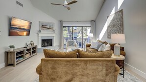 Una sala de estar moderna con chimenea, ventilador de techo y un ventanal grande con vista a una terraza.