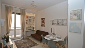 Een woonkamer met een bruine bank, een eettafel gedekt met borden en glazen, een kroonluchter en een boekenkast met diverse spullen.