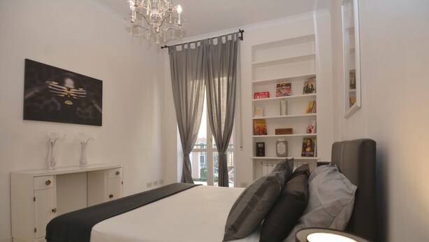 Een moderne slaapkamer met een groot bed, een nachtkastje, een boekenplank en een kroonluchter.