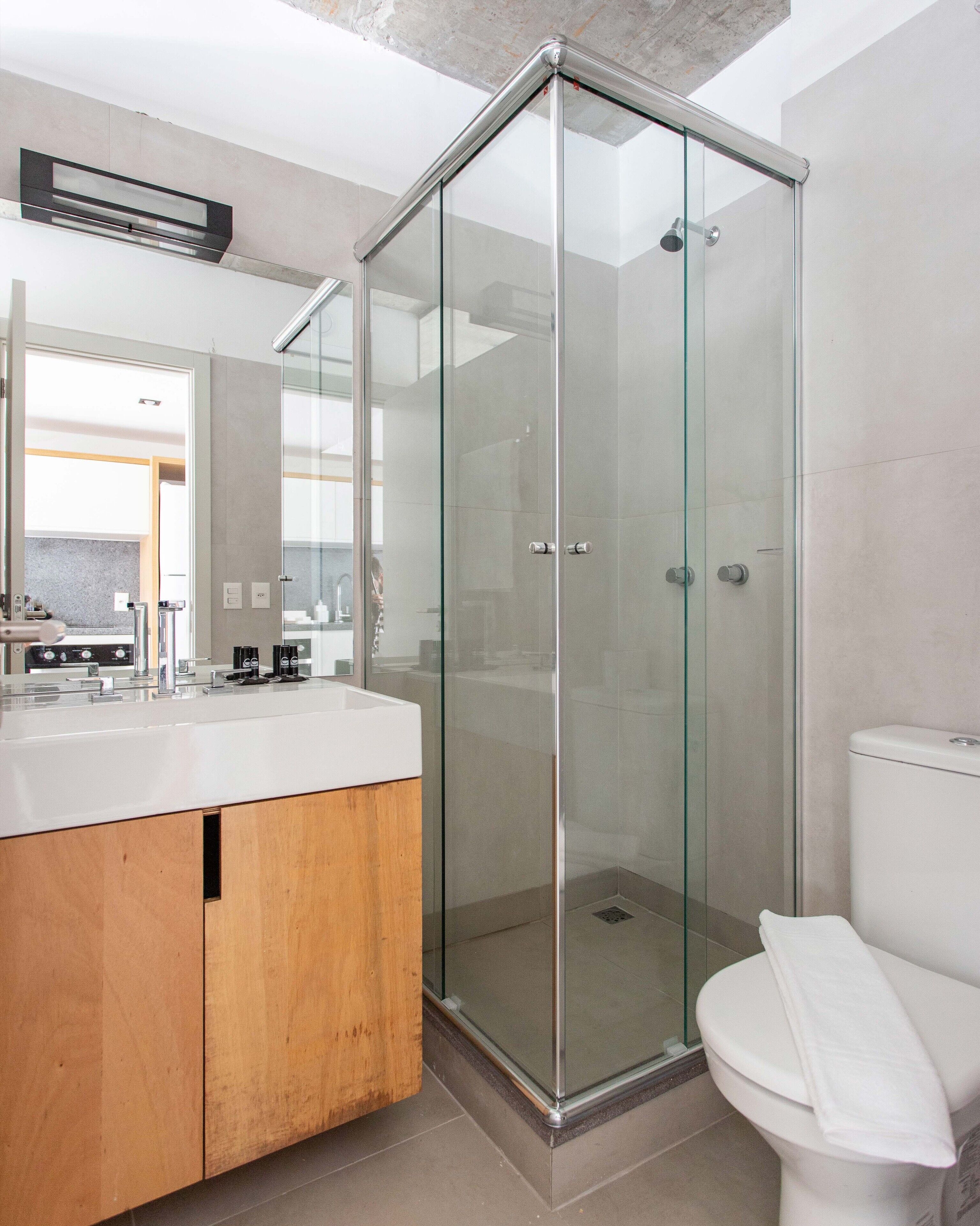 Un baño moderno con cabina de ducha de vidrio, un inodoro blanco y un mueble de tocador de madera.