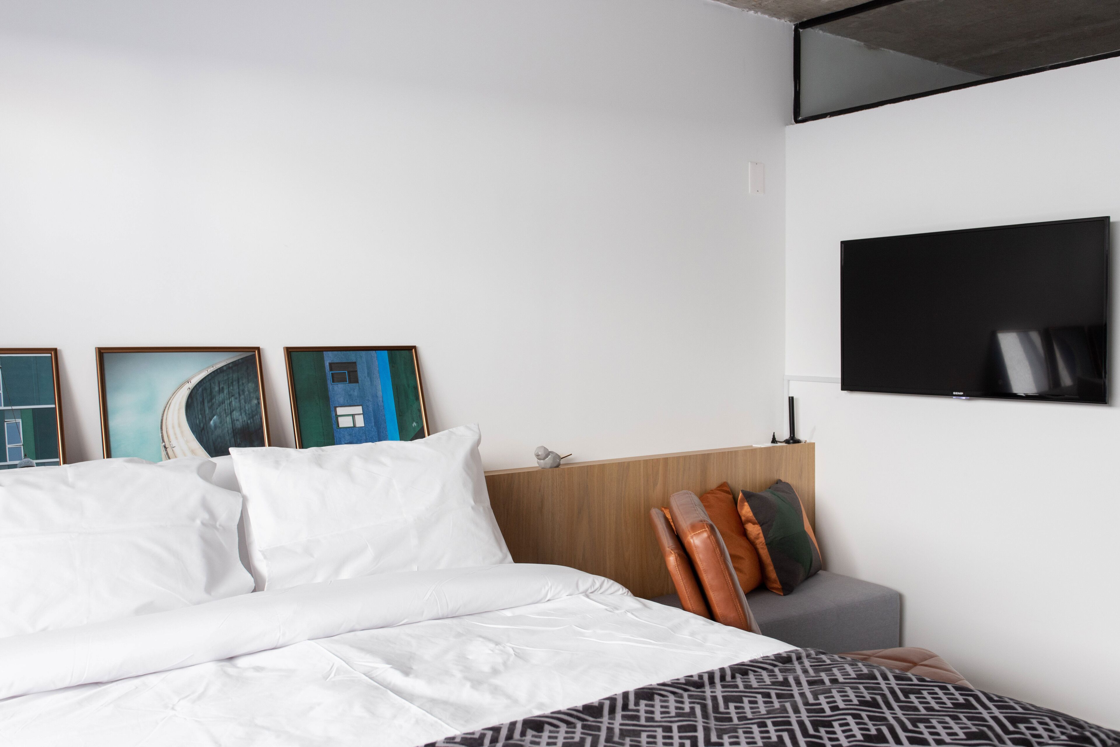 A modern hotel room with a large bed, a flat-screen TV mounted on the wall, and framed artwork on the wall.