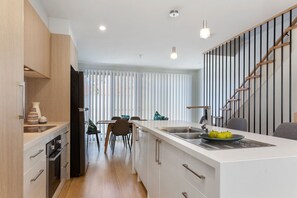 A modern kitchen with a central island, wooden cabinets, and a staircase leading to an upper level.