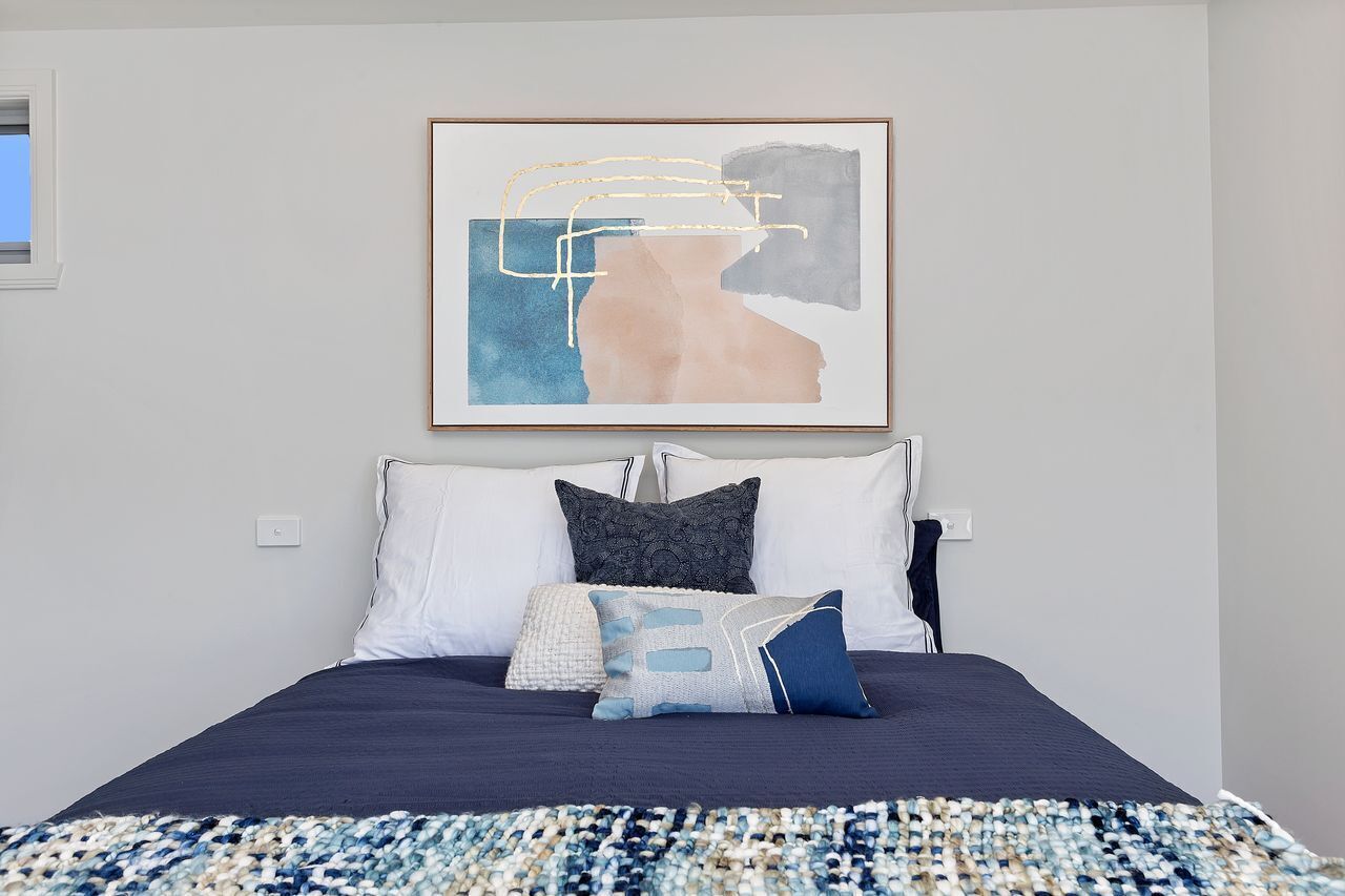Une chambre à coucher avec un lit, des oreillers, une couverture et un tableau abstrait encadré accroché au mur.
