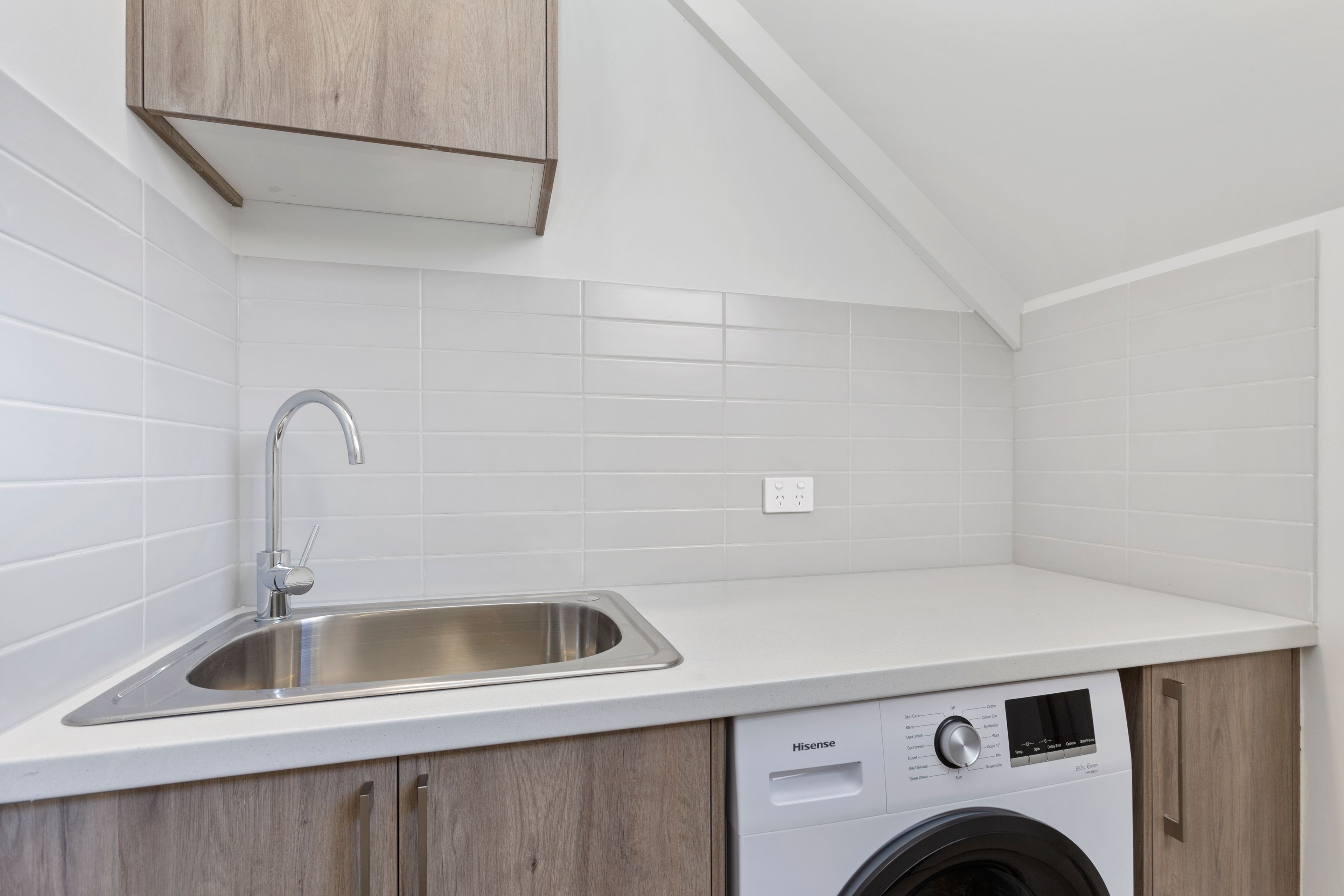 Una cocina compacta con un lavamanos de acero inoxidable, lavadora y armarios de madera.