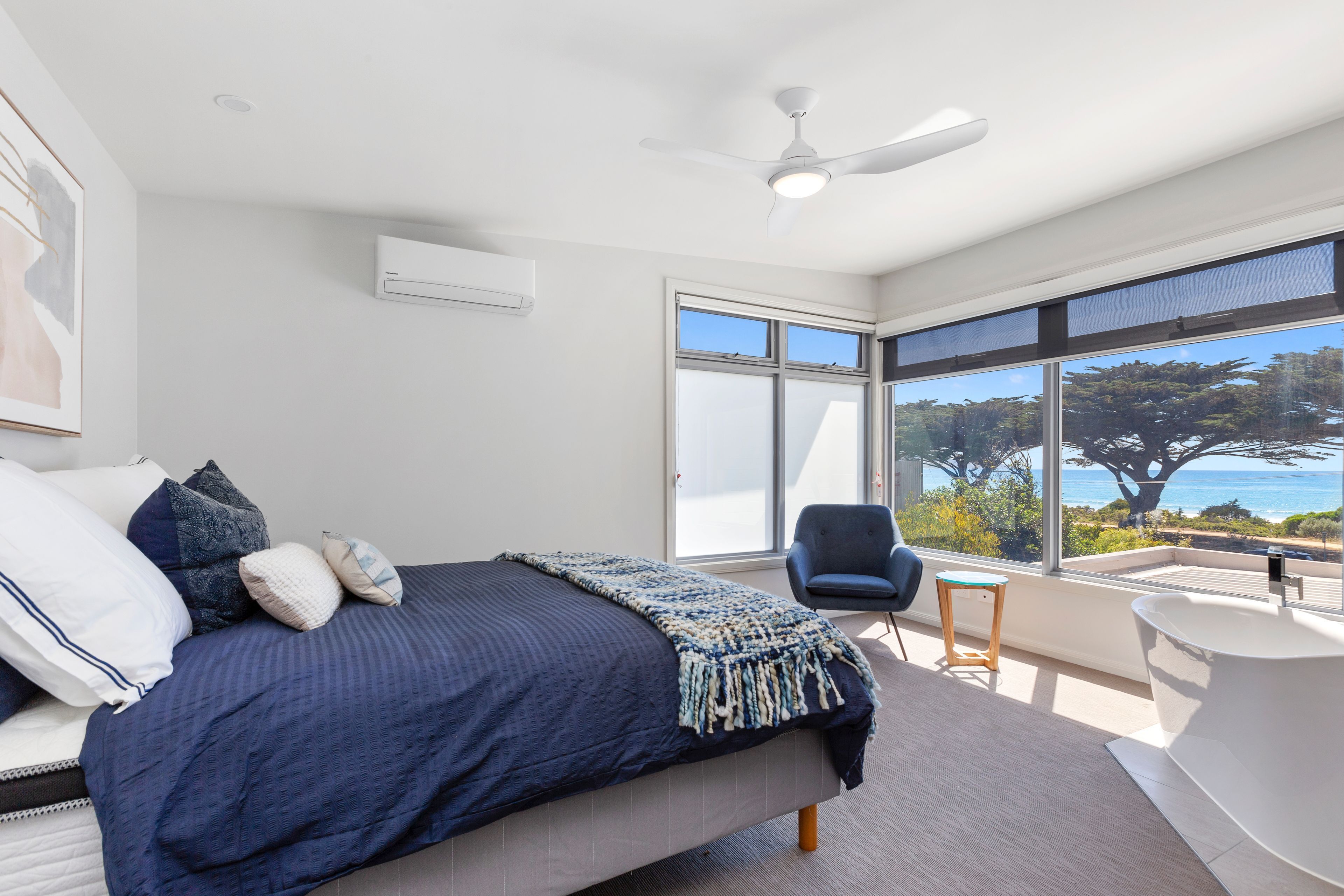 Une chambre à coucher avec un lit, une chaise, une grande fenêtre et un ventilateur de plafond.