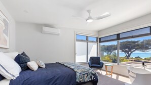 Ein Schlafzimmer mit Bett, Stuhl, großem Fenster und Deckenventilator.