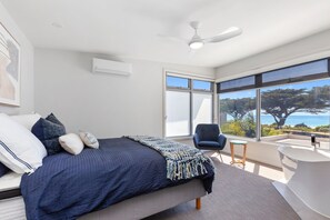 A bedroom with a bed, a chair, a large window, and a ceiling fan. - Seaside Apartment 5 Beachfront Location Apollo Bay (APOLLO BAY)
