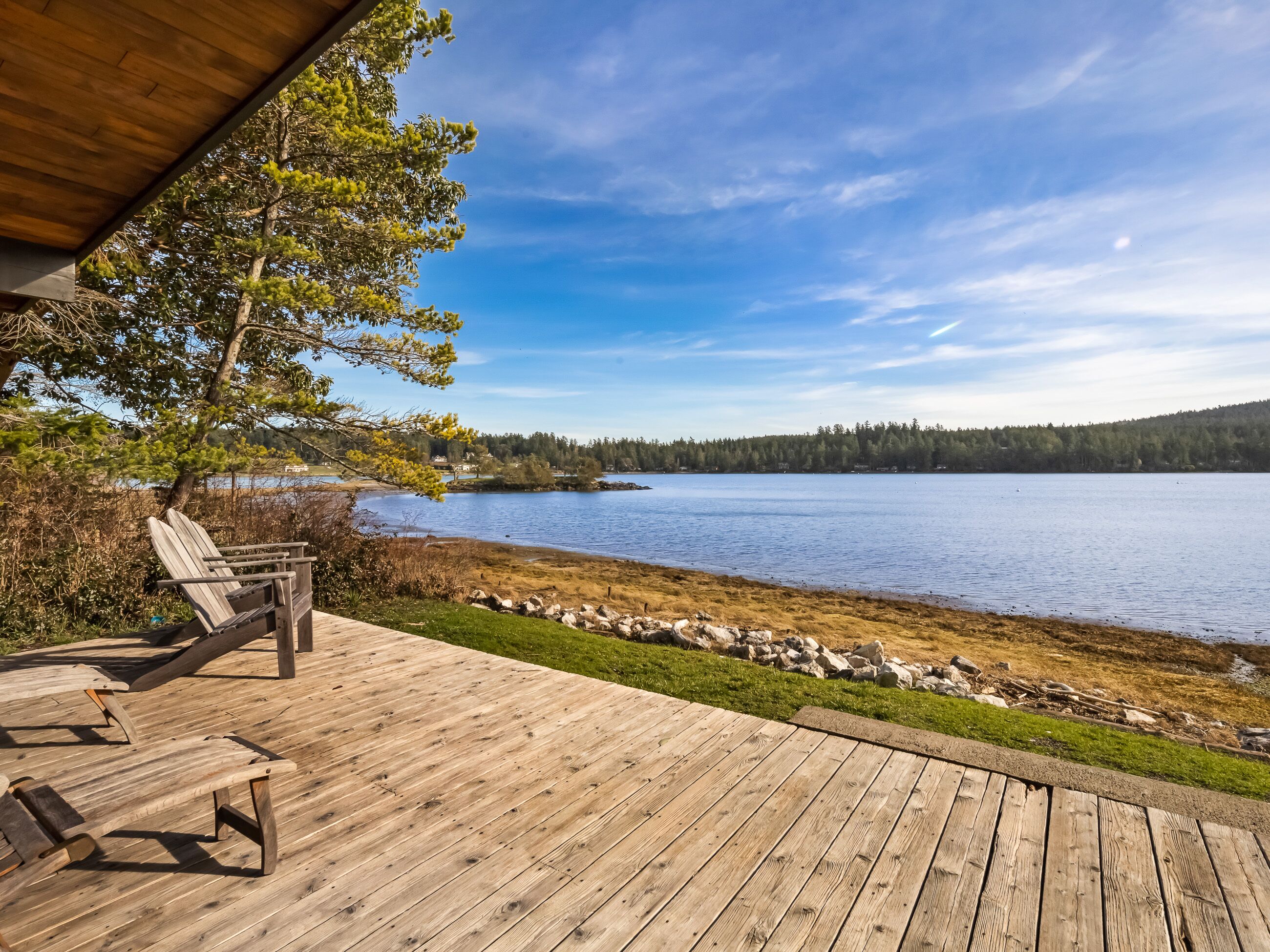 A wooden deck with two lounge chairs overlooking a lake, surrounded by trees and a clear sky.