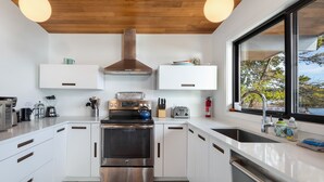 A modern kitchen with stainless steel appliances, white cabinetry, and a large window offering a view of trees and water. - Waterfront Home! Newly Remodeled! (weow) (Friday harbor)