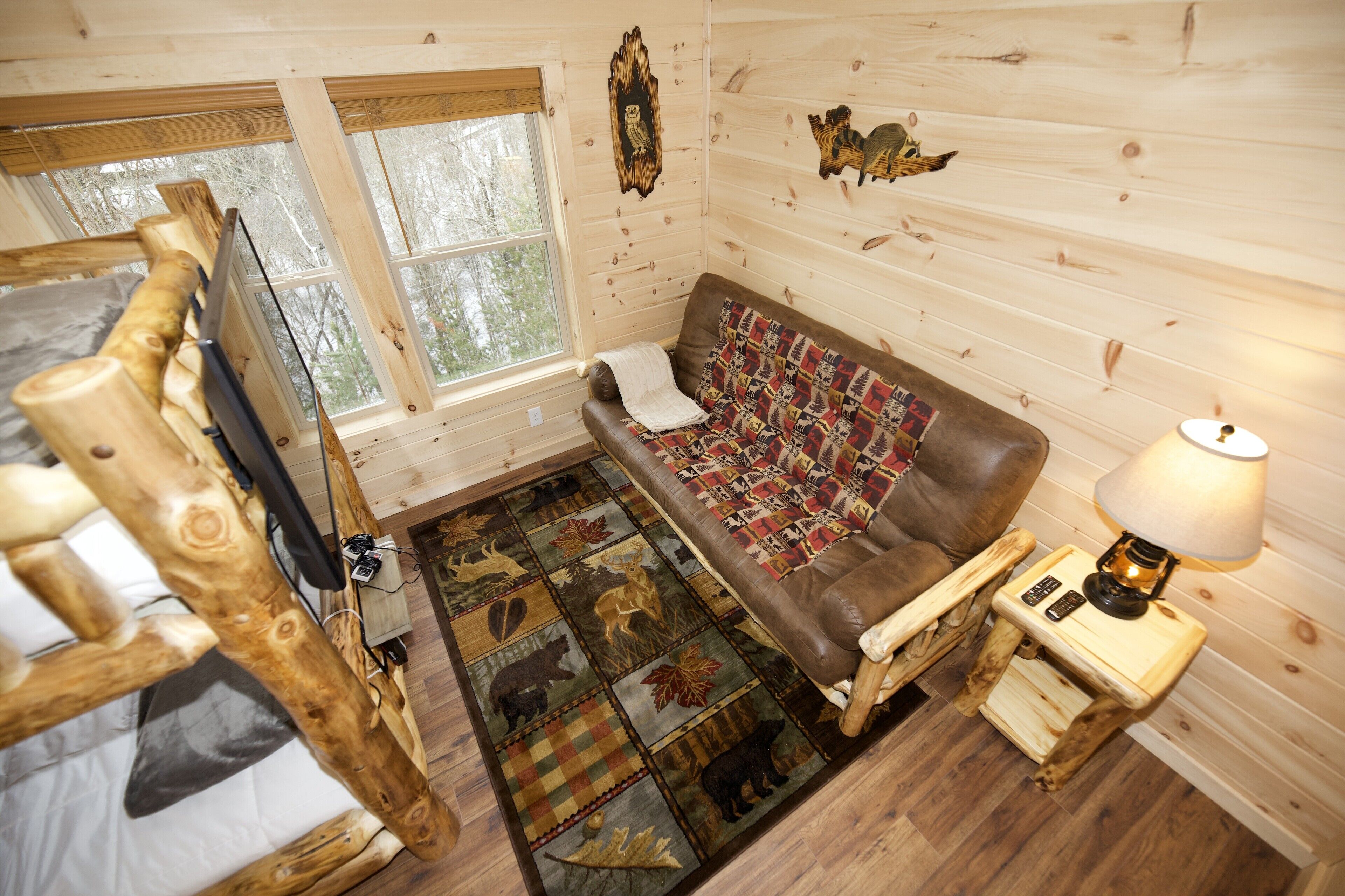 Ein gemütliches Blockhausschlafzimmer mit Holzboden, einem braunen Ledersofa, einem gemusterten Teppich, einem kleinen Nachttisch mit Lampe und einem Fernseher auf einem Holzgestell.