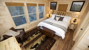 A wooden cabin bedroom with a bed, two bedside tables, a bench, a rug, and large windows. - Quiet Family Cabin on Private Mountain Top-Awesome Location! (Sevierville)
