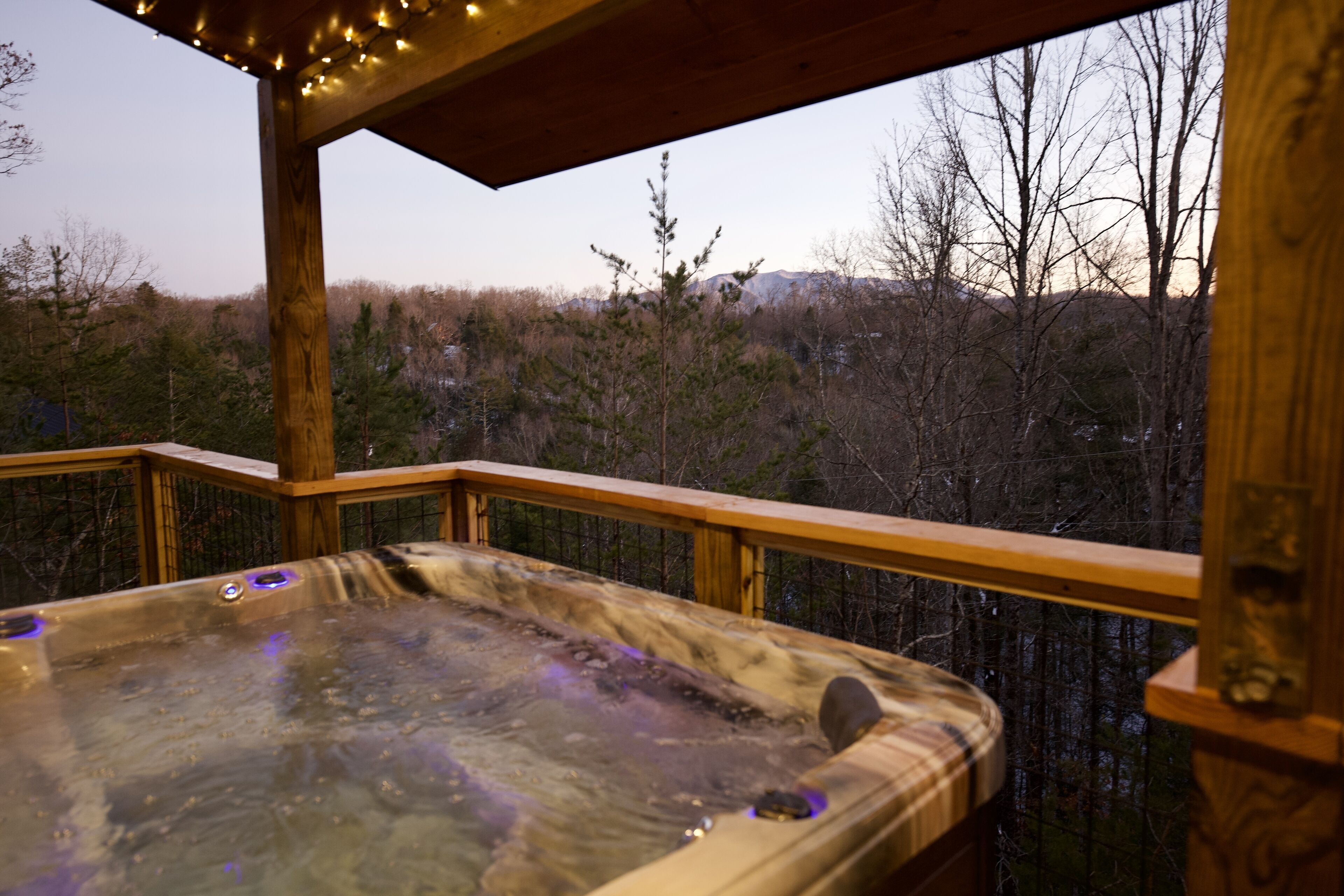 A hot tub on a wooden deck with a view of a forested area.