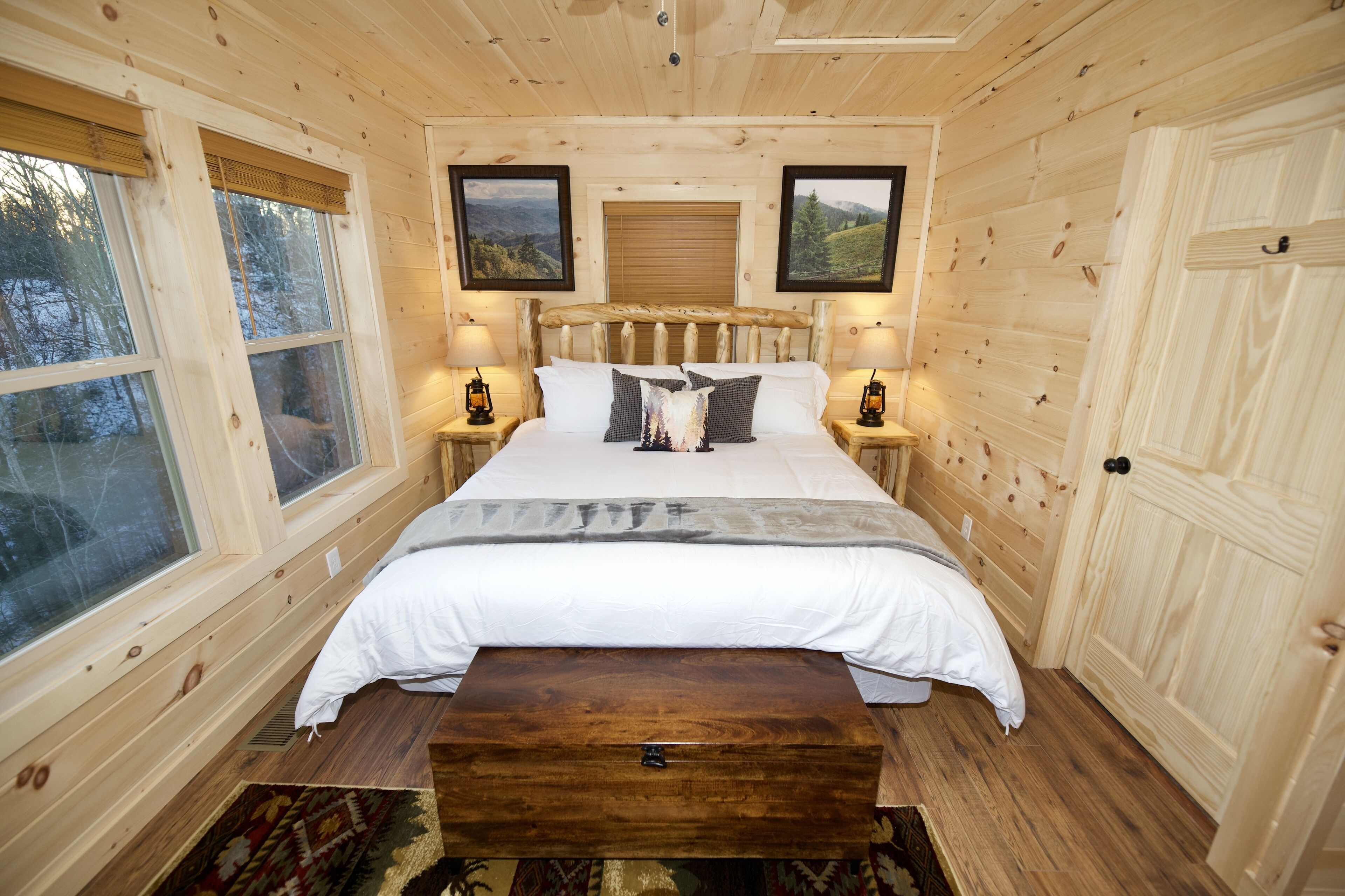 Ein Schlafzimmer einer Holzhütte mit einem Bett, zwei Nachttischen und zwei Fenstern.