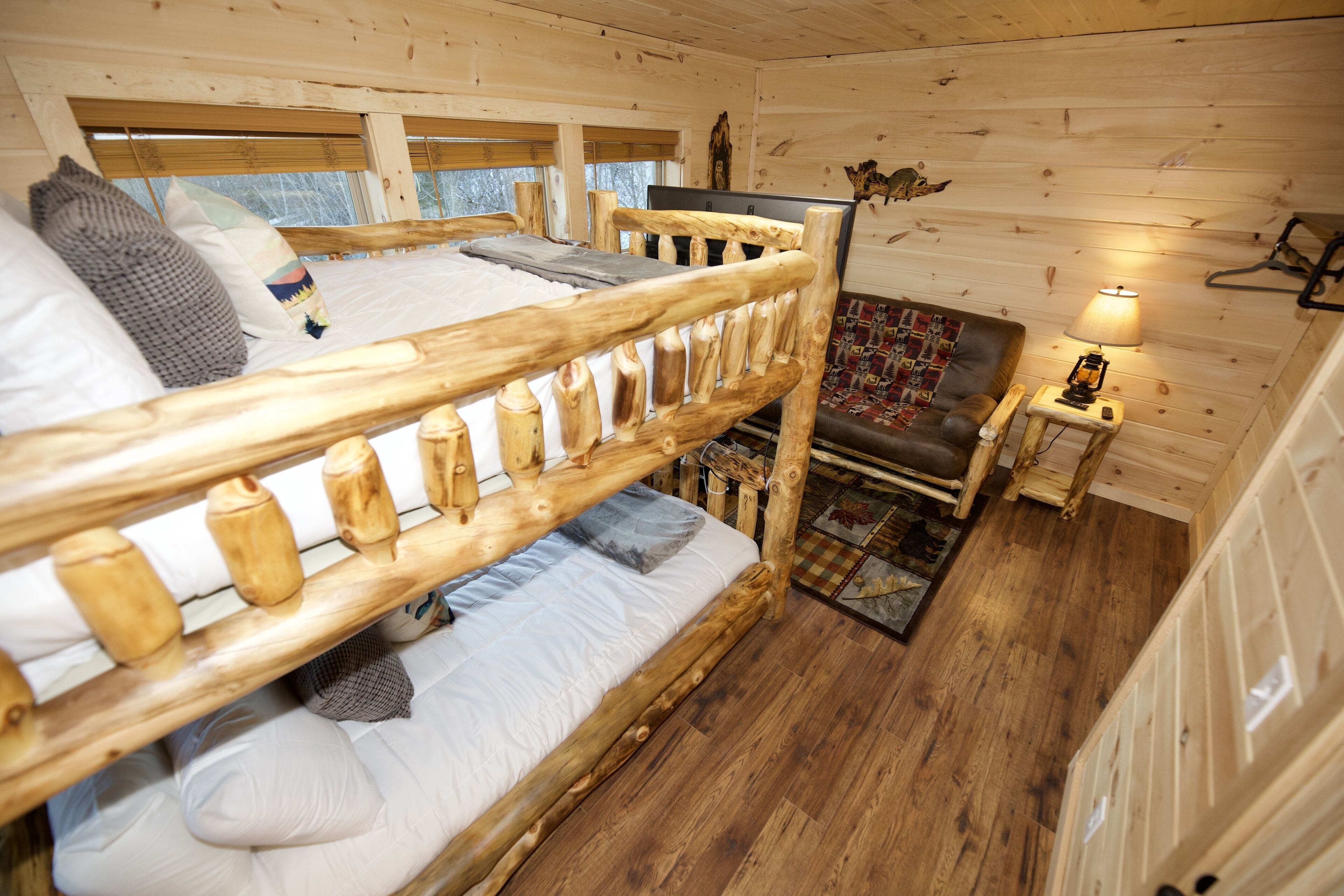 Una habitación tipo cabaña de madera con una litera, un sofá pequeño, una lámpara y una alfombra.