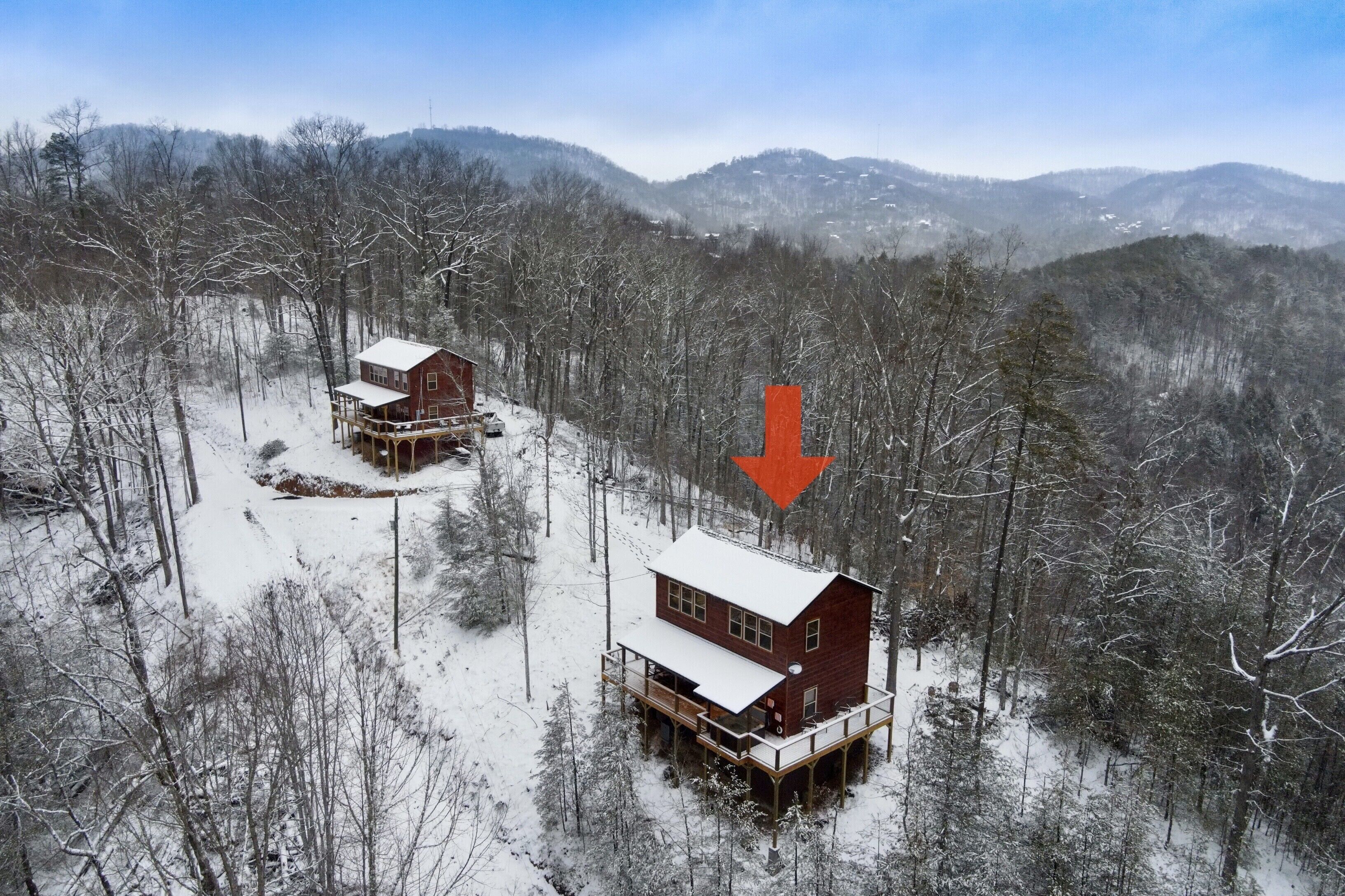 A cabin with a deck and a separate building, surrounded by a snowy forest.