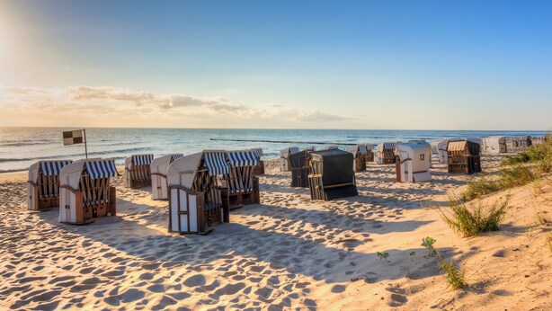 Strandhutten met gestreepte luifels en een vlag, gerangschikt op een zandstrand met de oceaan op de achtergrond.