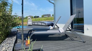 Een terras met loungebedden, een zwembad en een fles water.