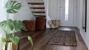 Een modern interieur met een houten trap, een potplant, een geweven vloerkleed en een deur met uitzicht.