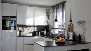 Een moderne keuken met witte kasten, een centraal eiland met zitplaatsen, een inbouwoven en een raam met blinds.