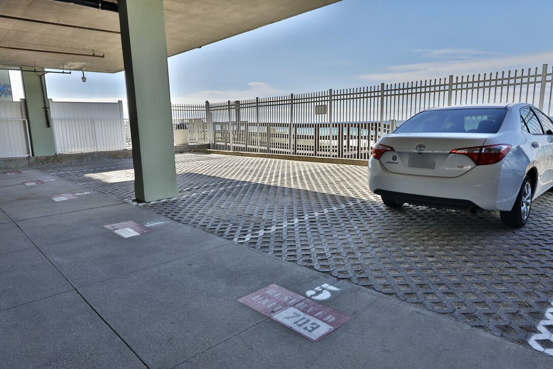 Un espace de stationnement avec une voiture blanche, des piliers en béton et une clôture métallique.