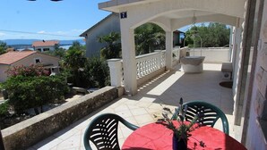 A terrace with a table and chairs, a view of the sea, and a building with a number 7 sign.