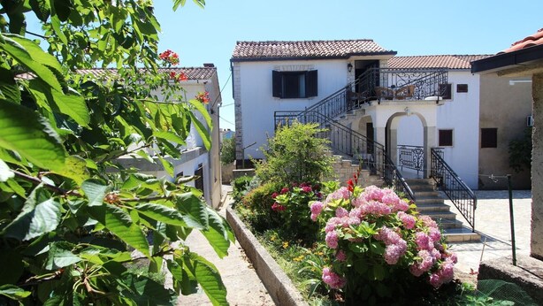 A courtyard with a staircase leading to a building with a tiled roof and a balcony.