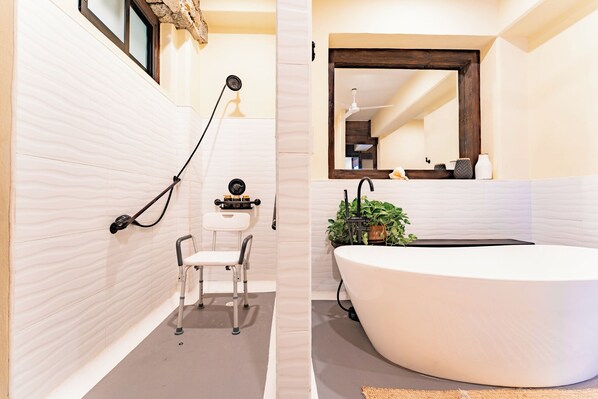 Une salle de bain moderne avec une grande baignoire, une petite table avec une chaise et un miroir au-dessus du lavabo.
