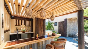 A bar area with a wooden counter, wicker chairs, and hanging wicker lamps.