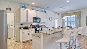 A kitchen with white cabinets, a microwave, a stove, and a large island with bar stools.