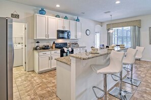 A kitchen with white cabinets, a microwave, a stove, and a large island with bar stools.