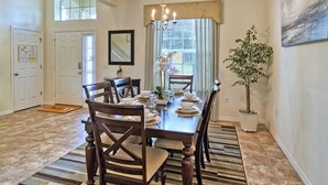 A dining room with a wooden table set for four, a chandelier, and a potted plant.
