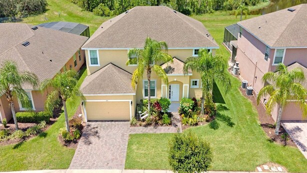 A two-story residential building with a garage, surrounded by well-maintained lawns and palm trees.