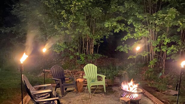 An outdoor seating area with chairs and a fire pit, surrounded by trees.