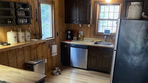 A wooden cabin kitchen with a dishwasher, refrigerator, and wooden cabinets.