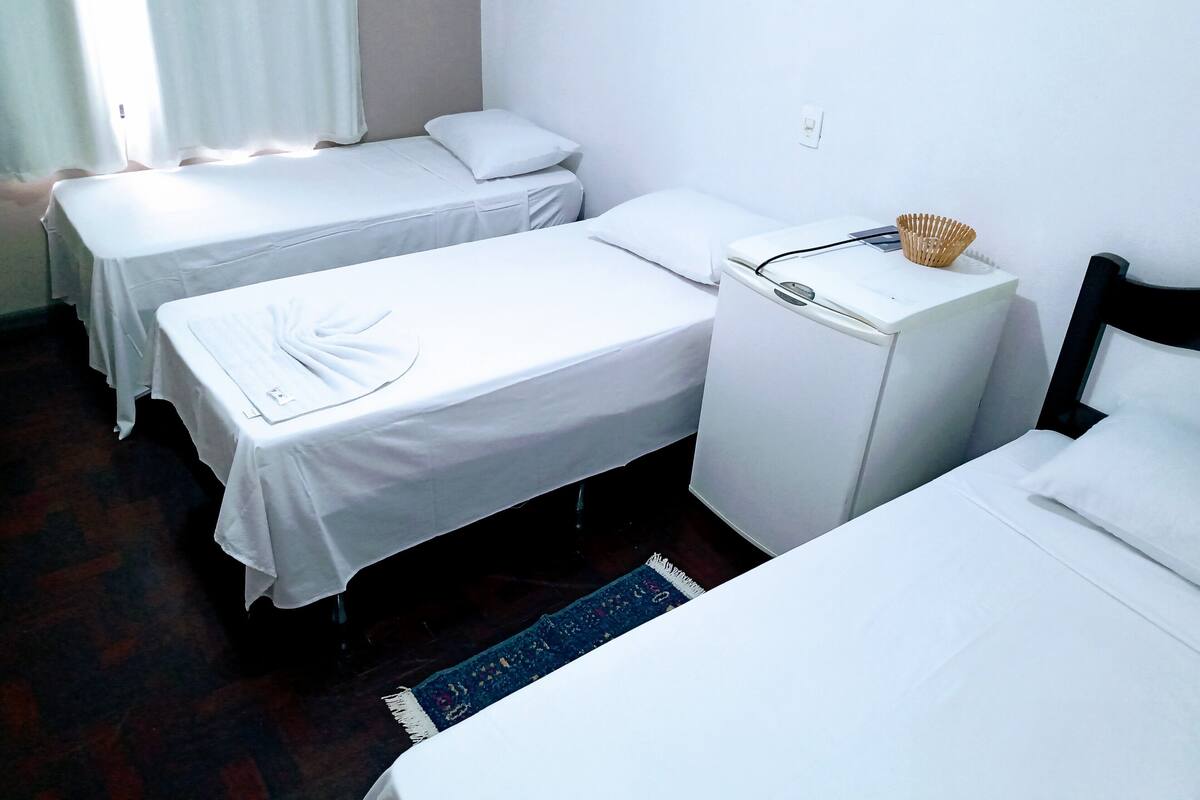Hotellihuone, jossa on kaksi erillistä sänkyä, pieni valkoinen jääkaappi ja sininen matto.