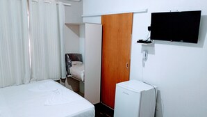 A hotel room with a bed, a small refrigerator, a wooden door, and a mounted TV. - Hotel Bless (Cascavel)
