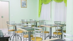 A classroom with tables and chairs, a framed picture on the wall, and green curtains. - Hotel Bless (Cascavel)