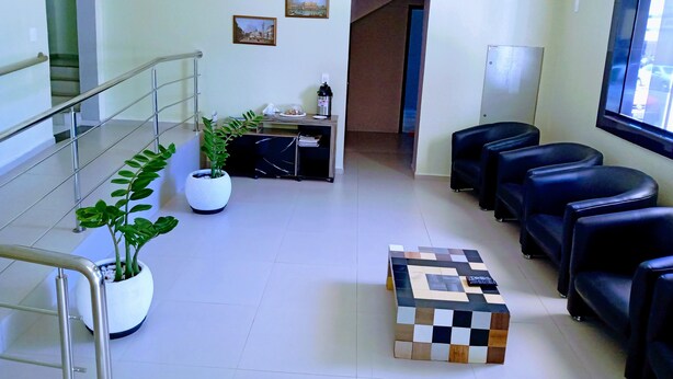 A reception area with a staircase, a reception desk, a potted plant, a check-in counter, and black leather seating. - Hotel Bless (Cascavel)