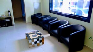 A waiting area with black leather chairs, a checkered coffee table, and a window with a view of parked cars. - Hotel Bless (Cascavel)