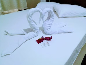 A bed with two white towels arranged in a swan shape, a small card, and two red packets on the bed. - Hotel Bless (Cascavel)