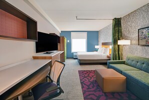 Una habitación de hotel con cama, escritorio, televisor, sofá y alfombra estampada.