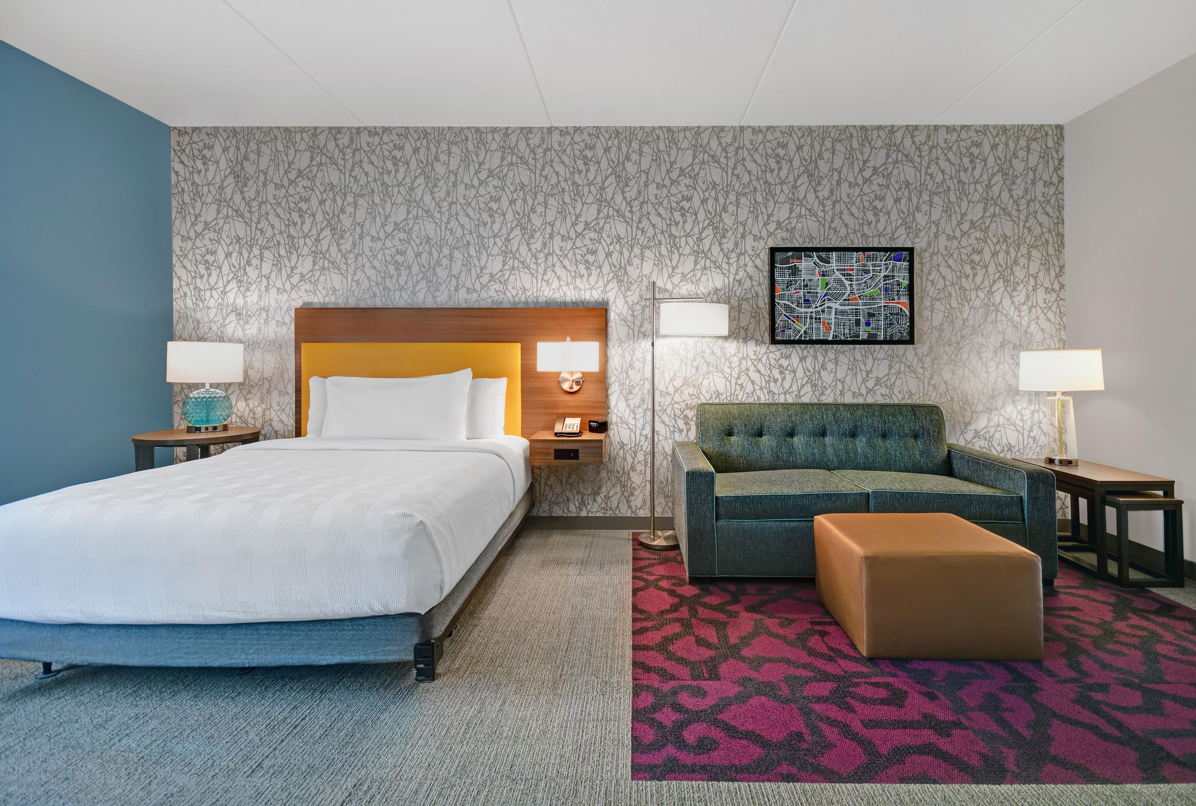 A hotel room with a bed, a sofa, a chair, a small table, and a wall-mounted artwork.