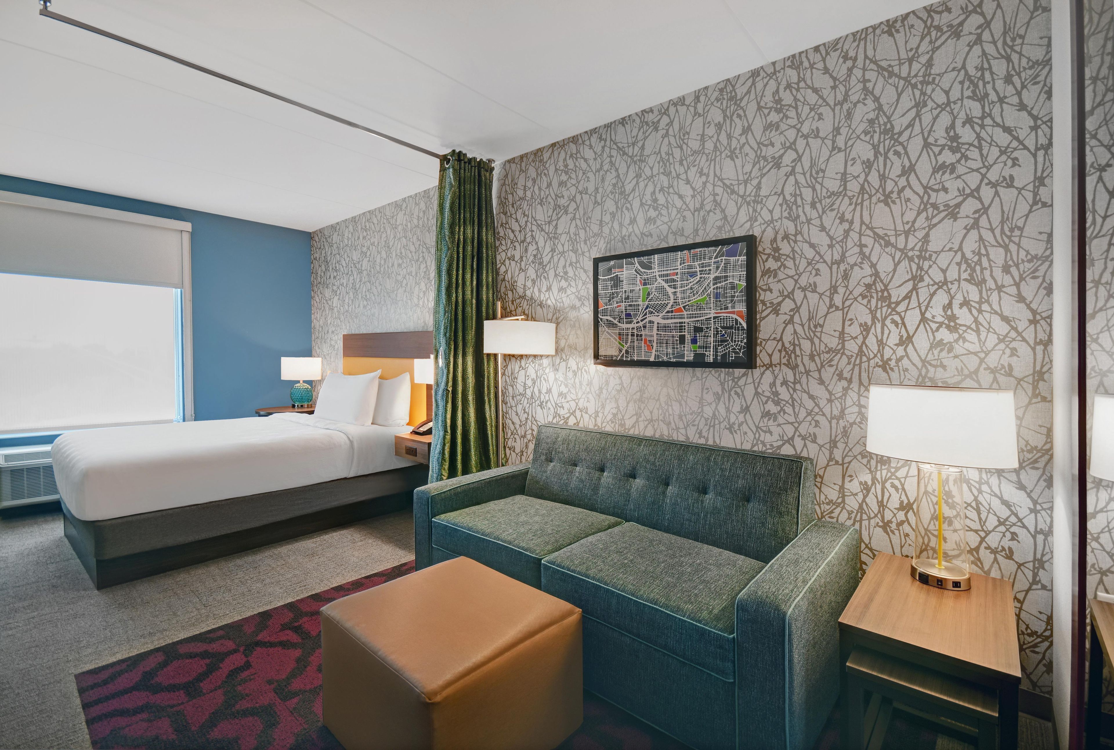 A hotel room with a bed, a sofa, a small table, and a wall-mounted map.