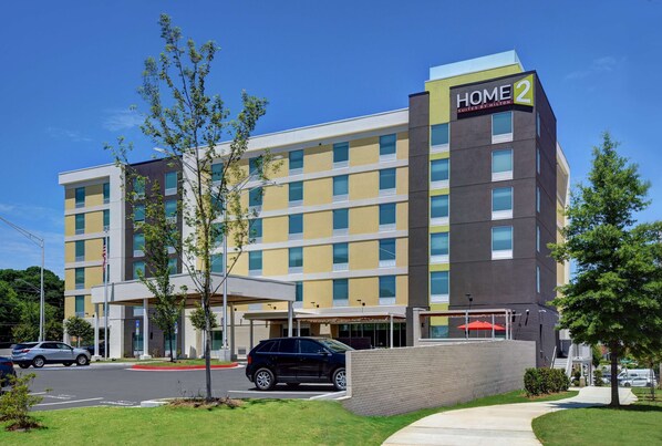 Un hôtel à plusieurs étages, reconnaissable à son grand panneau « HOME 2 », doté d’une entrée couverte et d’un parking où sont stationnées des voitures.