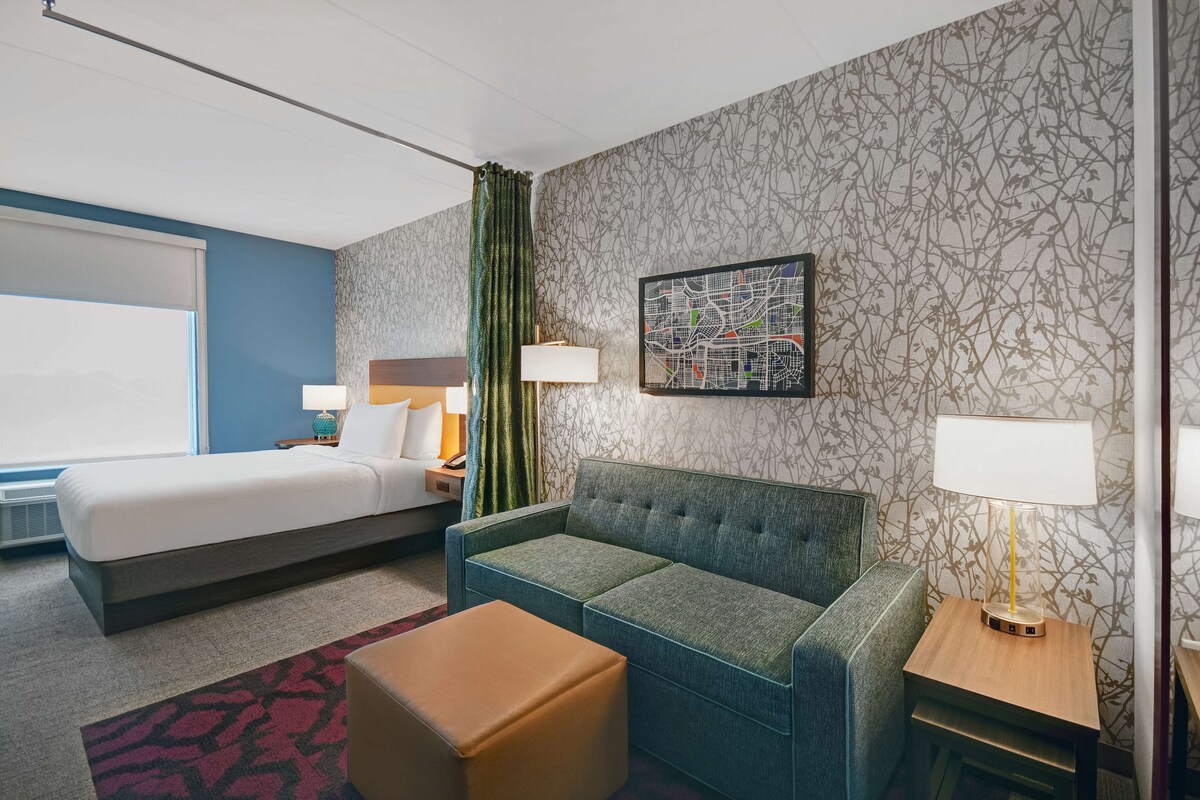 Una habitación de hotel con una cama, un sofá, una mesita y una lámpara.