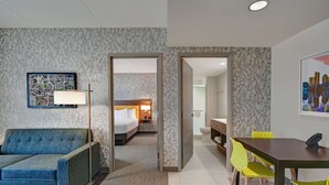 A hotel room with a sofa, a bed, a dining table with chairs, and a bathroom visible through an open door. - Home2 Suites by Hilton Atlanta Airport North (Atlanta)