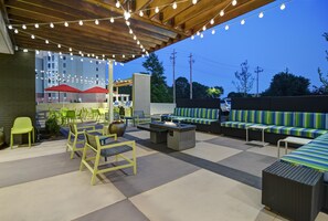 Un patio al aire libre con asientos, mesas y luces colgantes.
