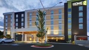 A multi-story hotel with a modern design, featuring a prominent "HOME 2 Suites by Hilton" sign, a covered entrance, and a landscaped area with a small tree. - Home2 Suites by Hilton Atlanta Airport North (Atlanta)