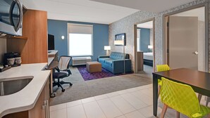 A modern hotel room with a kitchenette, a sofa, a dining table with chairs, and a large window providing natural light. - Home2 Suites by Hilton Atlanta Airport North (Atlanta)